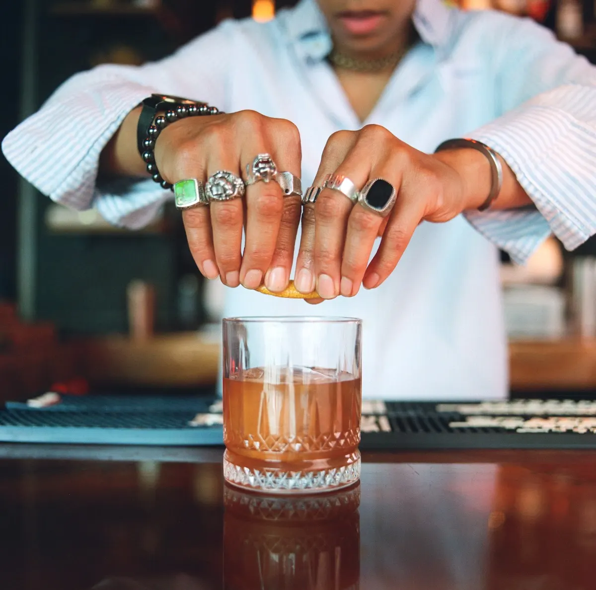 Hands squeezing citrus over a rocks glass at the bar